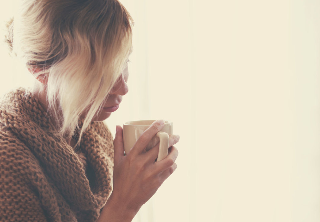 girl with blonde hair wearing a tan sweater and holding a mug