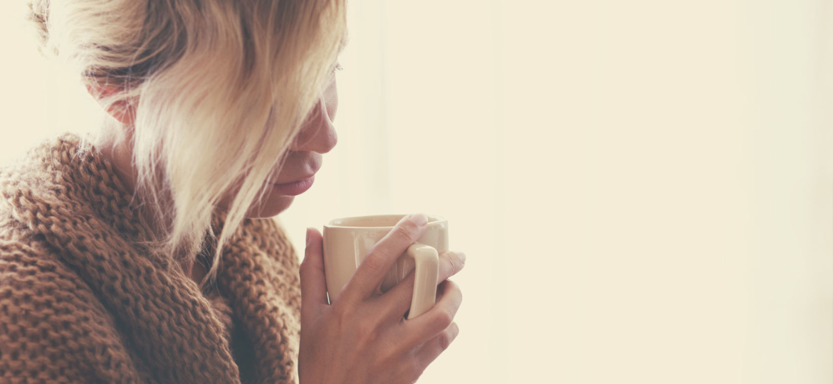 girl with blonde hair wearing a tan sweater and holding a mug