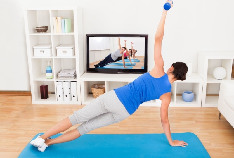 woman watching a workout video in her livingroom and doing a side plank on her yoga mat