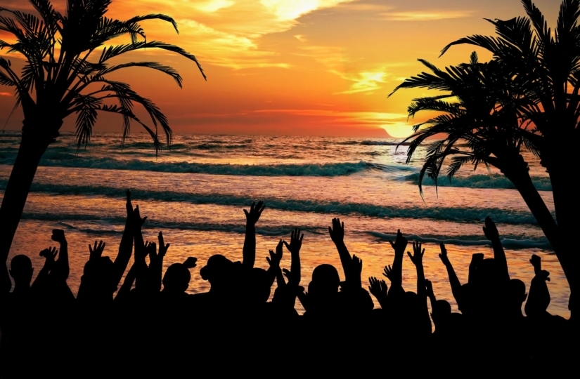 shadows of people partying on a beach with the sunset in the background