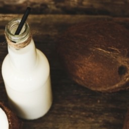 homemade coconut kefir in a bottle sitting on a wooden table beside a coconut