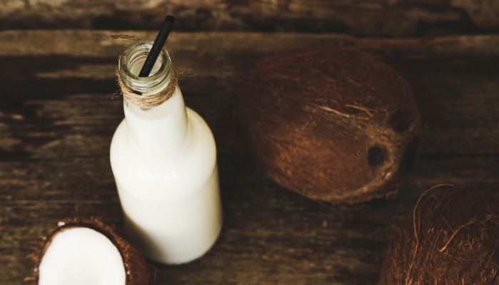 homemade coconut kefir in a bottle sitting on a wooden table beside a coconut