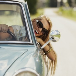 girl driving while hanging her head out the window, wearing sunglasses and smiling