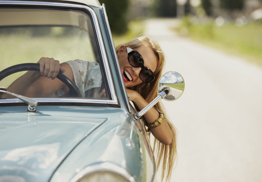 girl driving while hanging her head out the window, wearing sunglasses and smiling
