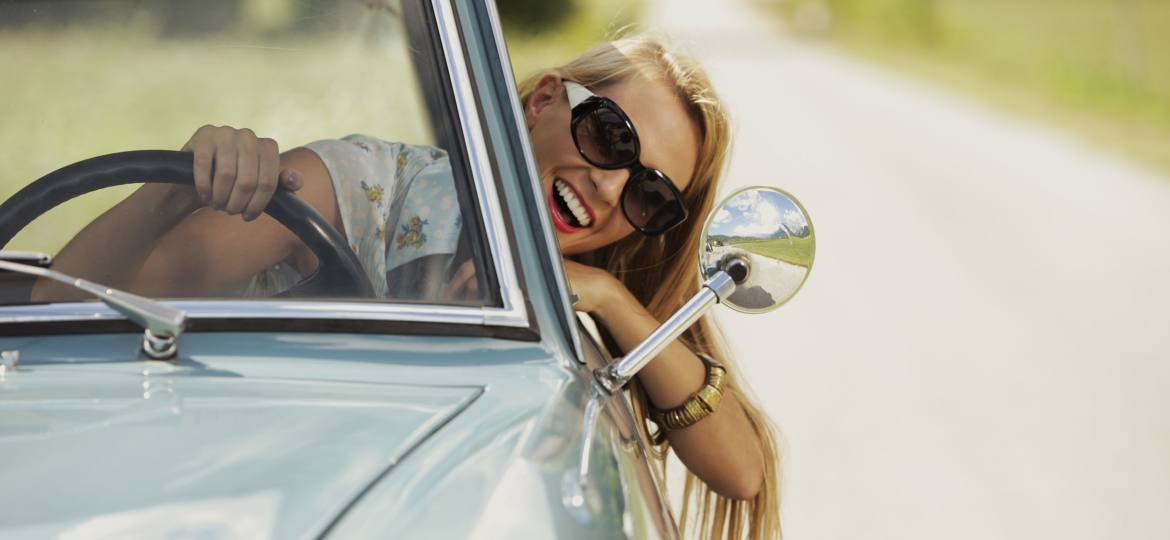 girl driving while hanging her head out the window, wearing sunglasses and smiling