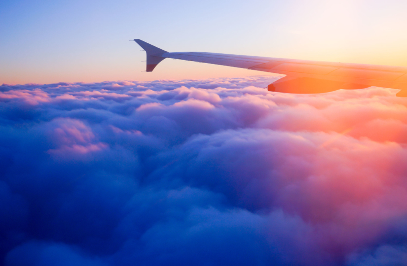 pic of plane wing while flying over the clouds into the sunrise