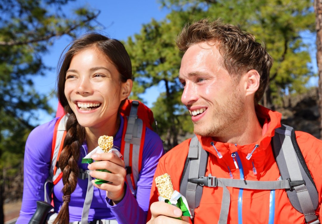 Man and woman hiking and eating a protein bar while hiking