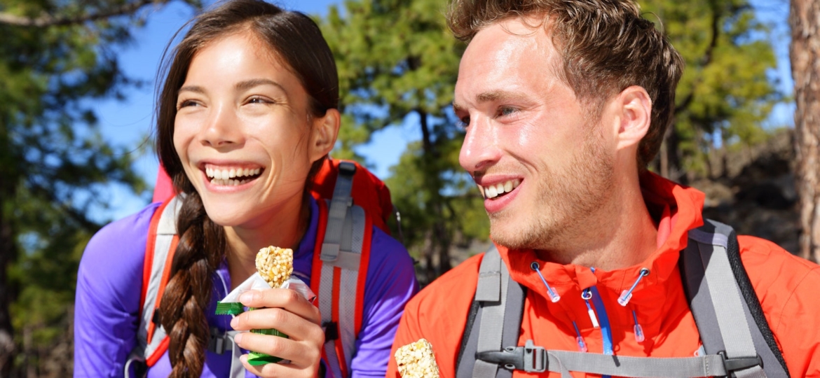 Man and woman hiking and eating a protein bar while hiking