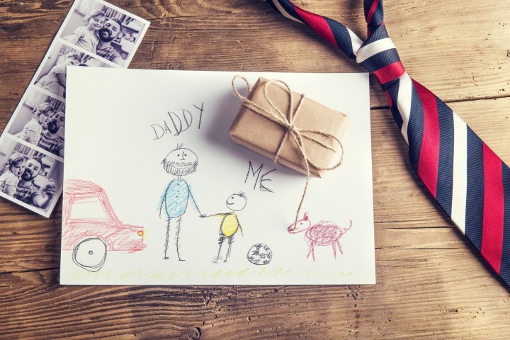 Picture of kids on white paper. Father's tie laying on table and a small wrapped gift.