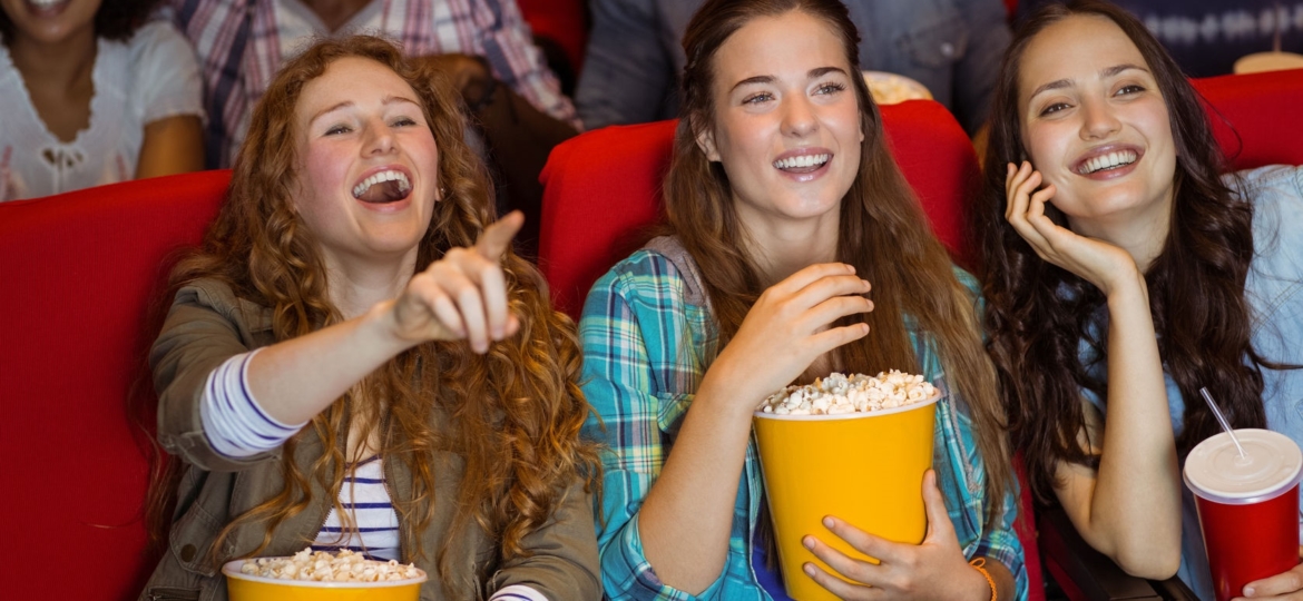 Three girls at the movie eating popcorn.